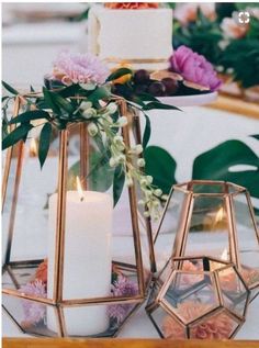 two candles are sitting on a table with flowers and greenery in front of them