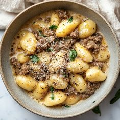 a bowl filled with pasta and meat on top of a white table cloth next to a spoon