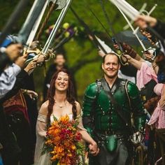 a man and woman dressed in medieval clothing walking down the street with swords on their heads