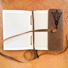 an open notebook with a pen on top of it next to a brown book strap