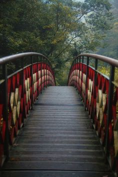 a wooden bridge with red railings and trees in the background