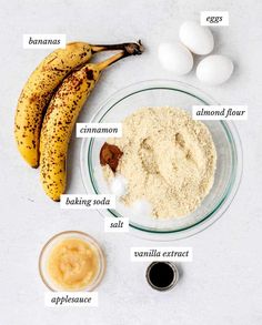 ingredients to make banana bread laid out on a white counter top, including bananas, flour, eggs and cinnamon