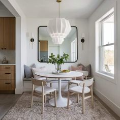 a dining room table with chairs and a large mirror hanging over it's head