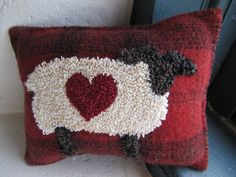 a red pillow with a sheep on it and a heart in the middle is hanging from a window sill