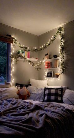 an unmade bed with christmas lights on the headboard