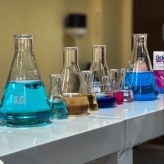 a row of glass flasks filled with blue liquid on top of a white counter