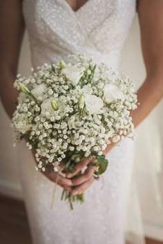 a woman in a wedding dress holding a bouquet of white roses and baby's breath