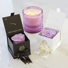 two roses in a gift box next to a candle on a marble counter top,