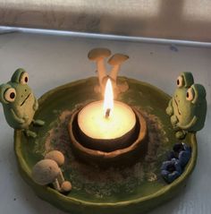 two frogs sitting on a plate with a lit candle in the middle and mushrooms around them