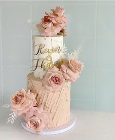 a three tiered cake with pink flowers on the top and gold lettering that says kauau keau