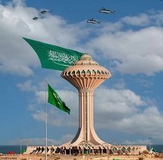 an air force jet flying over the top of a tall tower with flags in front of it