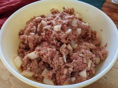 a bowl filled with meat and onions on top of a wooden table next to a red towel