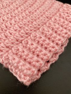 a pink crocheted blanket sitting on top of a black table next to a brown surface