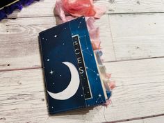 an open notebook with the moon and stars on it sitting on a wooden floor next to some tissue