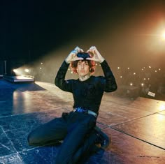 a woman sitting on the ground with her hands up to her head while wearing a hat