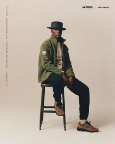 a man sitting on top of a wooden stool wearing a black hat and green jacket