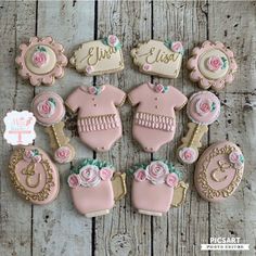 decorated cookies are arranged in the shape of baby's clothes and flowers on a wooden table