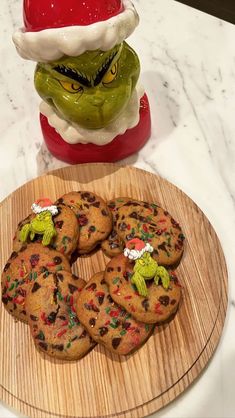 some cookies are on a wooden plate near a santa clause hat and an elf's head