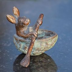 a bronze figurine sitting in a bowl with a wooden spoon on the table