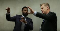 two men standing next to each other in front of a wall with their hands up