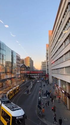 a yellow and white bus driving down a street next to tall buildings in the city