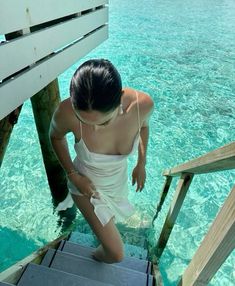 a woman in a white bathing suit standing on a dock over clear blue ocean water