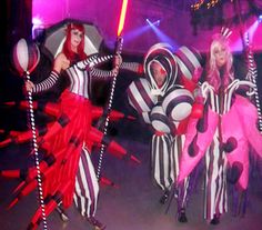 three women dressed in costumes and holding umbrellas are performing on stage with lights behind them