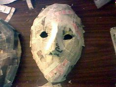 two masks made out of newspaper sitting on top of a wooden table