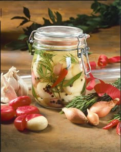 a glass jar filled with pickled vegetables on top of a wooden table next to garlic and pepper