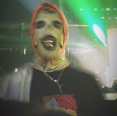 a man with his mouth open wearing a creepy mask and orange hair, on stage