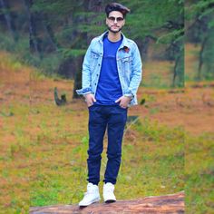 a man standing on top of a tree stump in the middle of a forest wearing a blue shirt and jean jacket