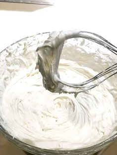 a glass bowl filled with whipped cream and a whisk