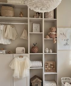 a baby's room with white shelves and clothes on top of them, including a teddy bear