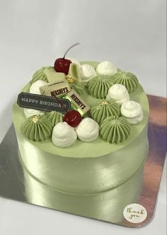 a green cake with white frosting and cherries on top