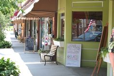 a woman standing on the sidewalk in front of a store with an american flag hanging from it's window