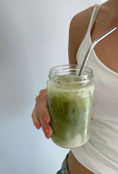 a woman holding a mason jar filled with green liquid and a spoon in her hand