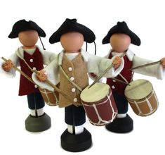 three wooden toy drummers with hats and drums on their heads, standing next to each other