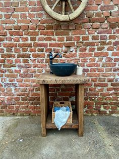 a sink sitting on top of a wooden table next to a brick wall with a wheel hanging above it