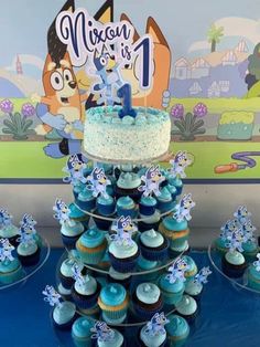 a cake and cupcakes are displayed on a table in front of a cartoon character backdrop