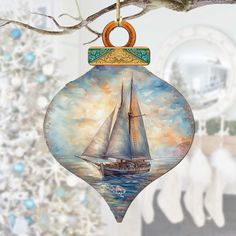 a glass ornament with a sailboat on the water in front of a christmas tree