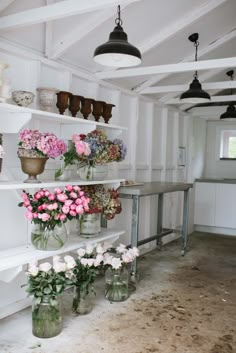 several vases filled with flowers sit on shelves in a white walled room next to a table