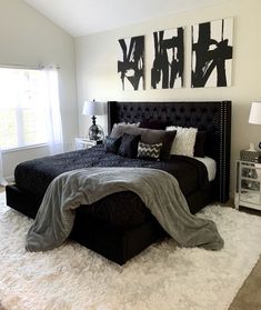 a black and white bedroom with two paintings on the wall above the bed, along with rugs