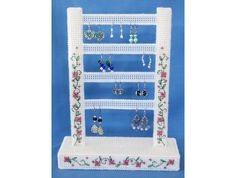 a crochet jewelry rack with earrings on it and flowers around the base, in front of a blue background