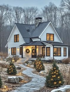 a white house with christmas lights on the front porch and trees in the back yard