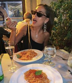 a woman sitting at a table with plates of spaghetti in front of her and wine glasses