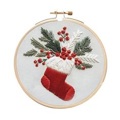 an embroidered christmas stocking with holly and red berries is hanging from a hoop on a white wall