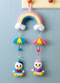 two little birds hanging from hooks with umbrellas and a rainbow in the sky above them