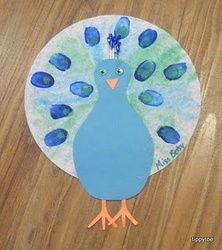 a paper plate with a blue and green peacock painted on it's side, sitting on a wooden surface