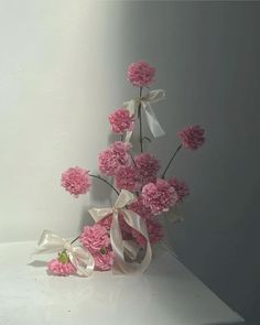 pink carnations and white ribbons are arranged in a vase on a countertop