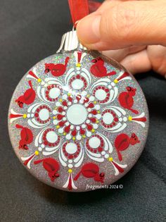 a hand holding a red and white ornament with birds on it's side